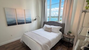 Ein Schlafzimmer mit einem Bett, einem Nachttisch, Blick aufs Wasser und drei Bildern an der Wand.