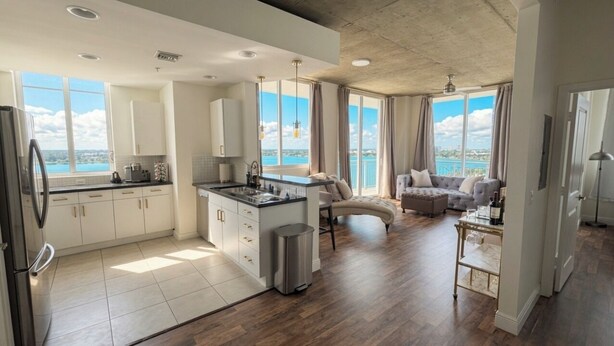 Eine moderne Küche mit einer zentralen Kochinsel, einem Essbereich mit einer Couch und großen Fenstern mit Blick auf das Meer.