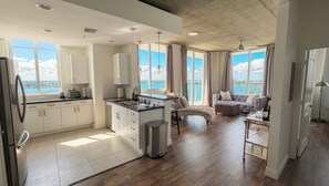 Una cocina moderna con una isla central, una zona de comedor con sofá y grandes ventanales con vistas al mar.