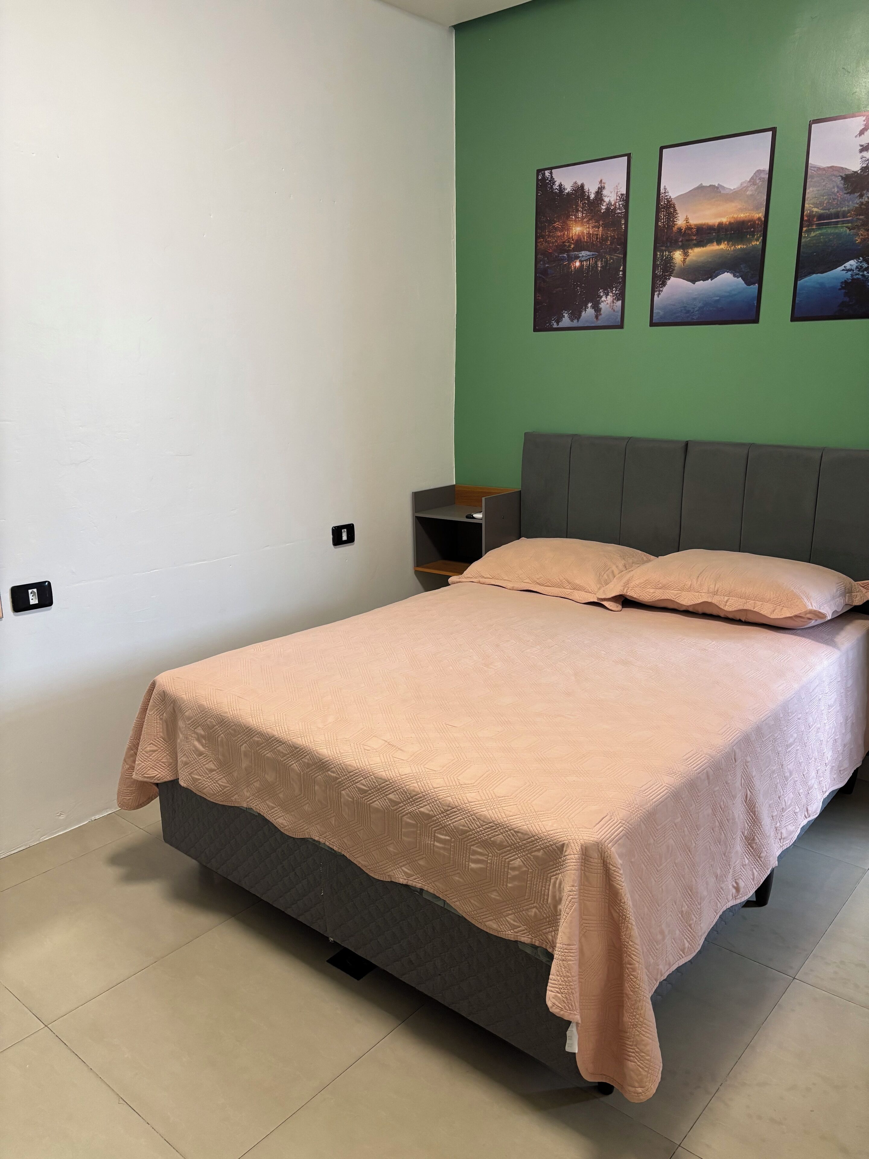Een slaapkamer met een bed, een nachtkastje en drie ingekaderde foto’s aan de muur.