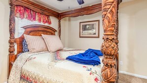 Una cama con dosel y doselera adornada con un edredón floral, un ventilador de techo e imagen enmarcada en la pared.