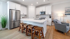 A modern kitchen with white cabinets, stainless steel appliances, a central island with stools, and a grey sofa in the adjacent living area. - Heated Salt Pool | Walk to Beach | Lowered Rates | Firepit (Port St. Joe)