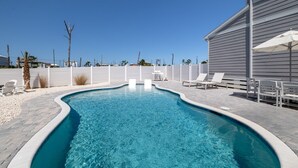 A swimming pool with a curved edge, surrounded by a white fence, and white lounge chairs. - Heated Salt Pool | Walk to Beach | Lowered Rates | Firepit (Port St. Joe)