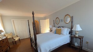 Een slaapkamer met een hemelbed, een houten dressoir, een stoel en twee nachtkastjes met lampen.