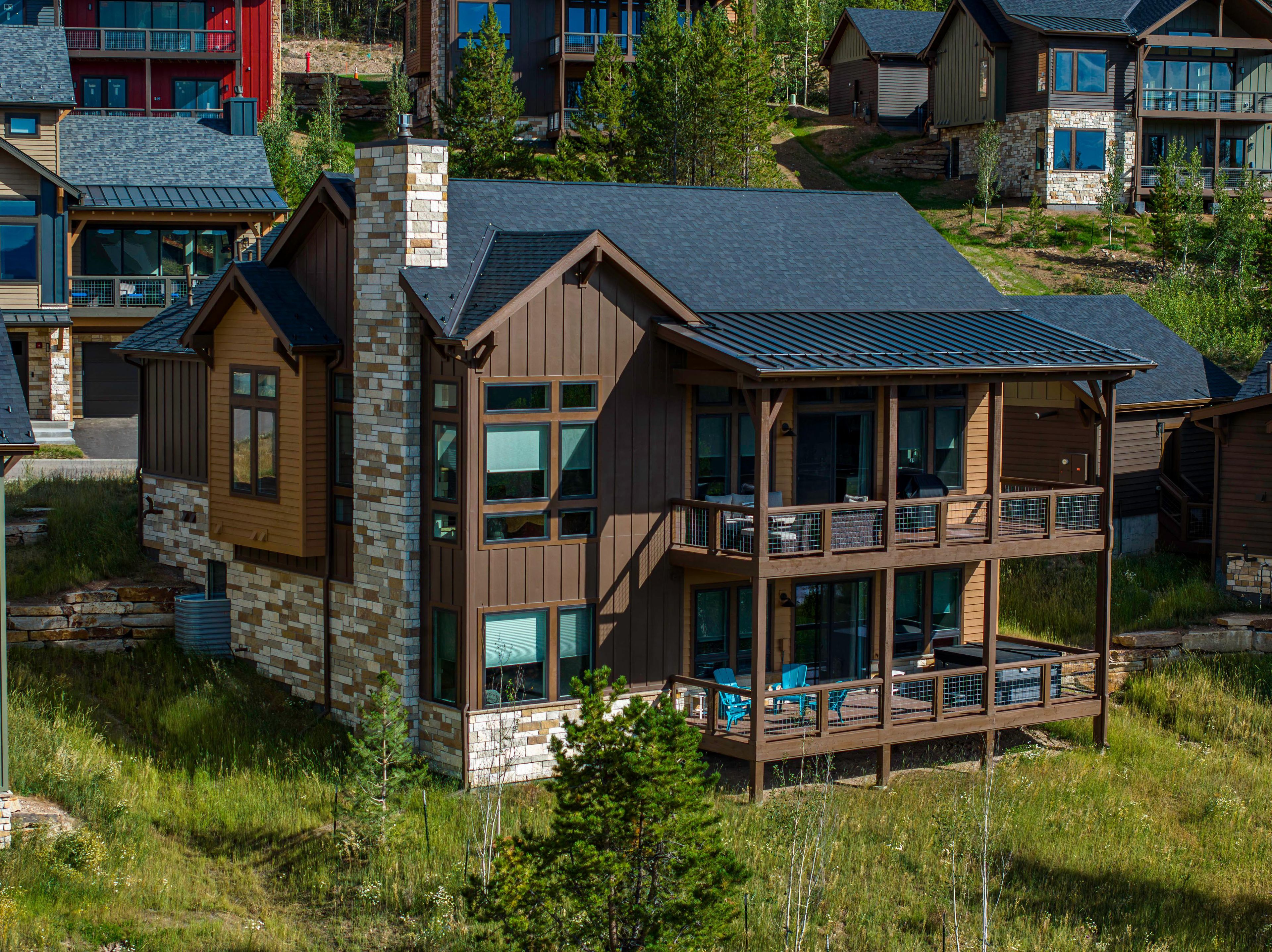 A multi-story wooden cabin with a balcony, surrounded by trees and other cabins.