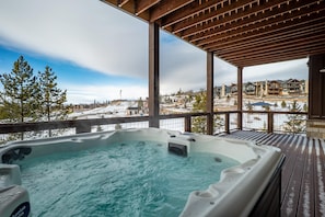 A hot tub on a wooden deck with a view of a snowy landscape and buildings. - Rendezvous 4BR Retreat | New Hot Tub, Mtn Views (Winter Park)
