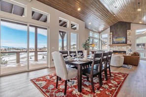 A spacious dining area with a large table set for six, surrounded by chairs, and a red patterned rug on the floor. - Rendezvous 4BR Retreat | New Hot Tub, Mtn Views (Winter Park)