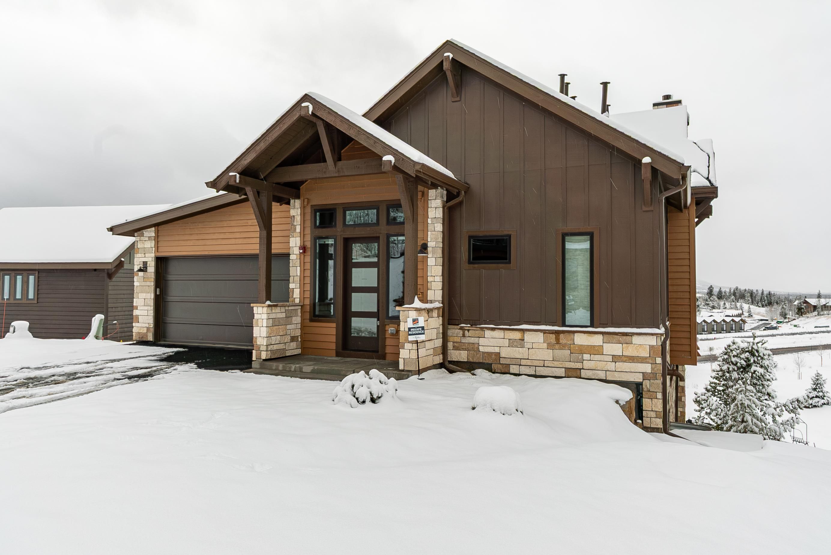 A two-story house with a garage, a front porch, and a snow-covered landscape.