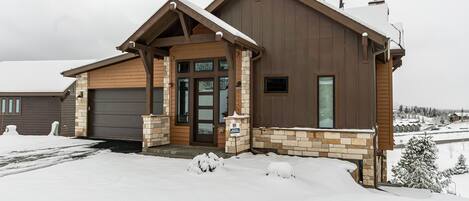 A two-story house with a garage, a front porch, and a snow-covered landscape.