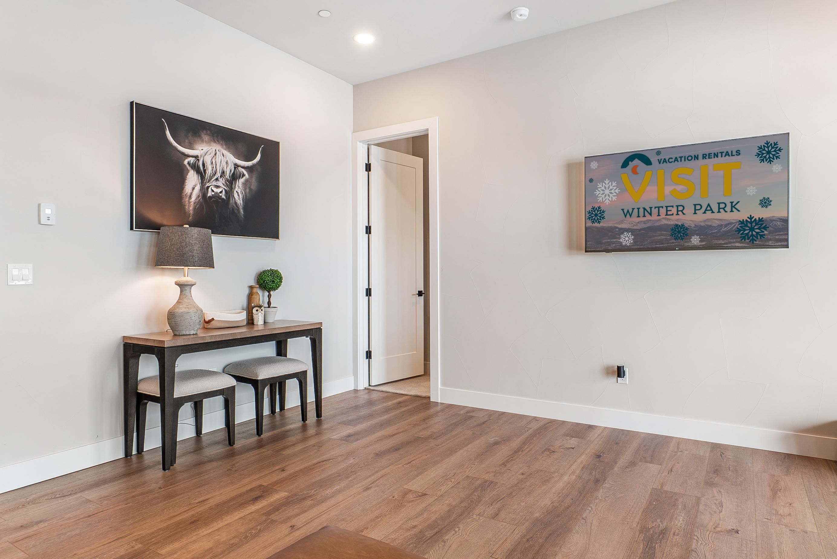 A modern interior with a wooden floor, a desk with two chairs, a lamp, and a framed picture of a bull.