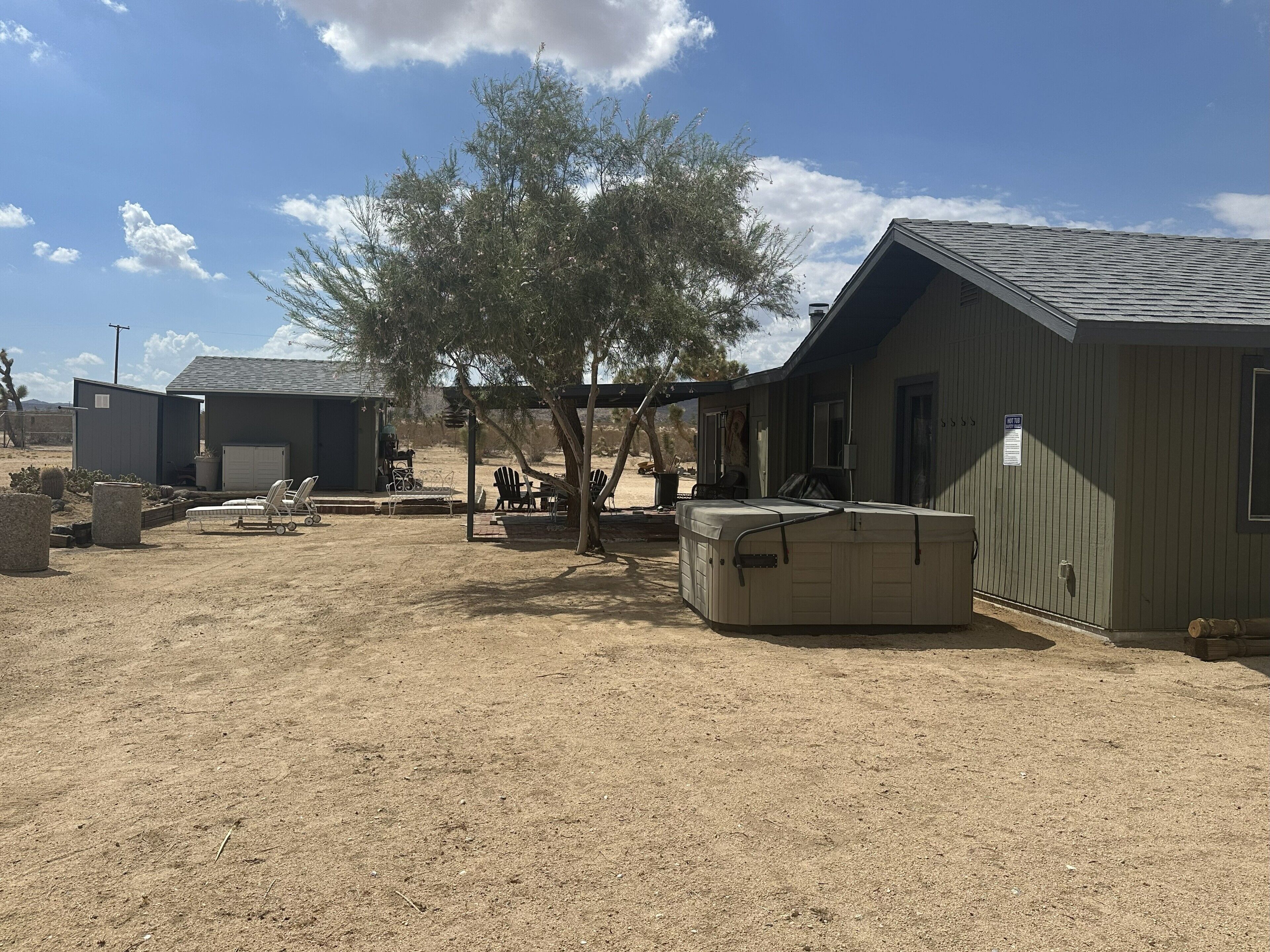 A rustic outdoor area with a covered seating area, a large water heater, and a small building with a garage.