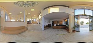 A spacious lobby with a curved staircase, a reception desk, and large glass doors leading outside. - Palmera Hotel (Kuşadası)