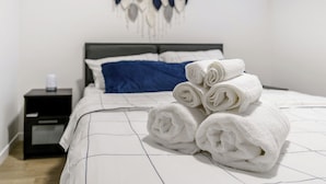 A neatly made bed with rolled white towels, a blue pillow, and a wall decoration. - CozyWolf (New 2 Bedroom Suite) (Calgary)