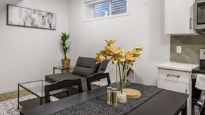 A modern kitchen with white cabinets, a black countertop, and a dining area with a table set for two. - CozyWolf (New 2 Bedroom Suite) (Calgary)
