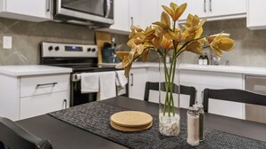 A modern kitchen with white cabinets, a microwave, and a stove. There is a table with a vase of yellow flowers and salt and pepper shakers. - CozyWolf (New 2 Bedroom Suite) (Calgary)