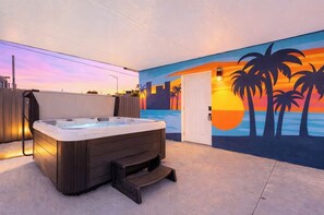 Uma banheira de hidromassagem em um quarto com um mural do pôr do sol, uma porta e uma cerca.