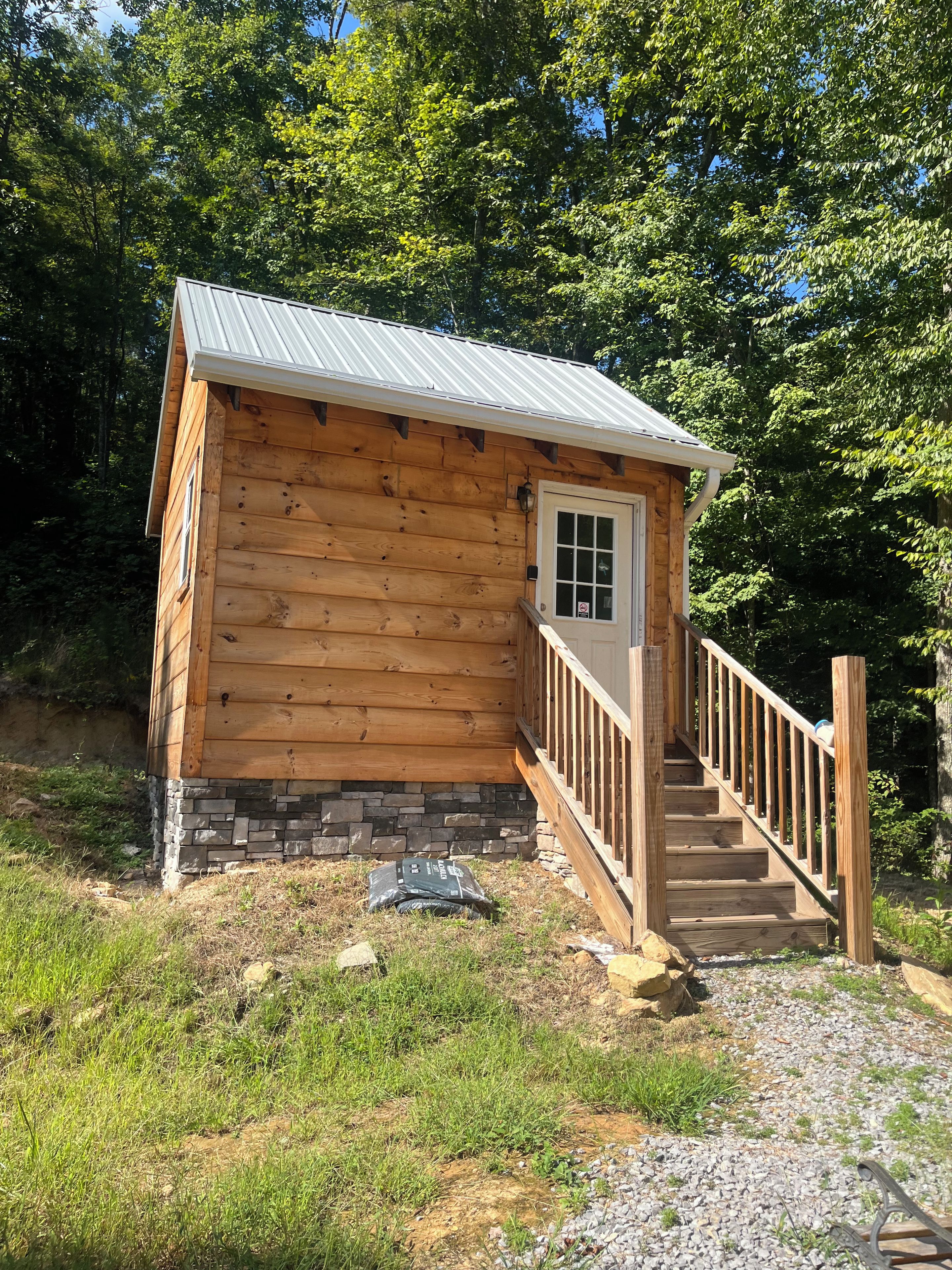 Une cabane en bois, avec des fondations en pierre, un toit en métal et un escalier en bois menant à une porte.