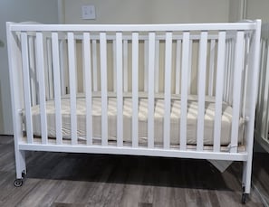 A white crib with a mattress, wheels, and a wall socket. - Kaweah Oaks Cabin: Firepit, Hot Tub, Game Room (Three Rivers)