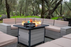 An outdoor seating area with a fire feature labeled 'S'Mores Station' and a brick-patterned table. - Kaweah Oaks Cabin: Firepit, Hot Tub, Game Room (Three Rivers)