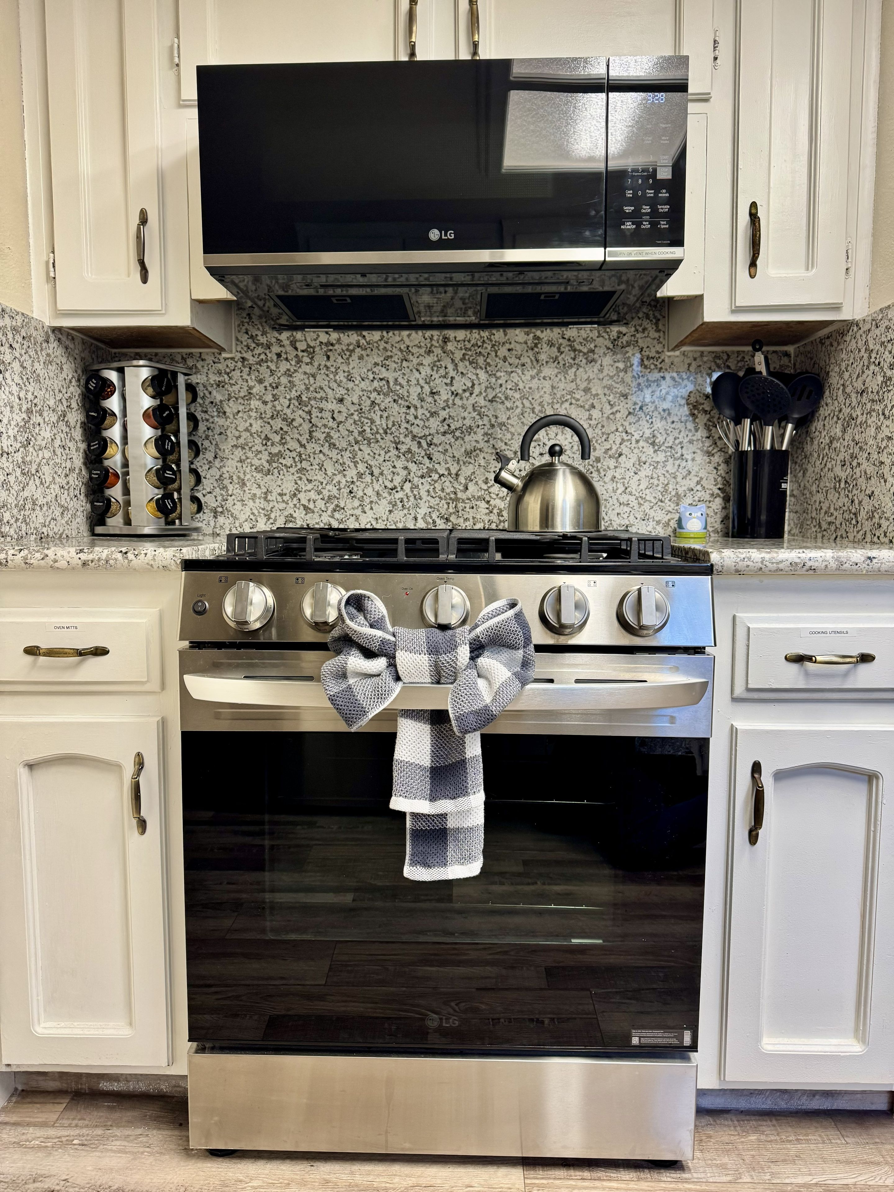 A kitchen with a stainless steel stove, a microwave above it, and a kettle on the countertop.