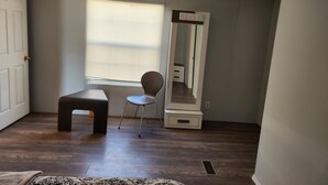 A room with a wooden floor, a bench, a chair, a large mirror, and a window with blinds. - The Zia Estate- Gated New Mexico Hideaway (Farmington)