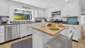 Une cuisine moderne avec des meubles blancs, un îlot central en bois et une fenêtre donnant sur la forêt.