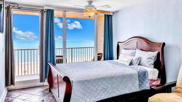 Ein Schlafzimmer mit einem Bett, einem Deckenventilator und Blick auf den Strand durch große Fenster.