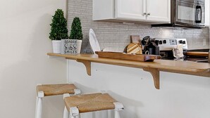 A kitchen with white cabinets, a wooden countertop, a microwave, and a toaster. There are two potted plants on the countertop.