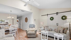 A living room with a sofa, chairs, a dining table, a ceiling fan, and a fireplace.