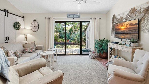 A living room with a ceiling fan, a sofa, a coffee table, a TV, and a view of the outdoors.