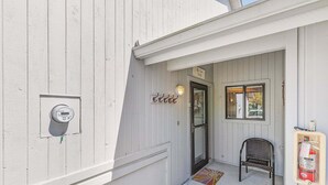 A white building with a door, a chair, a fire extinguisher, and a meter.