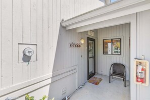 Un bâtiment blanc avec une porte, une chaise, un extincteur et un compteur.