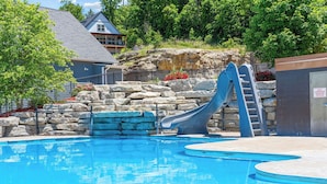 Une piscine avec un toboggan, des murs en pierre et un bâtiment en arrière-plan.