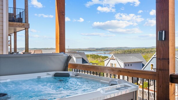 Un bain à remous sur une terrasse en bois, avec vue sur des maisons et un plan d’eau.