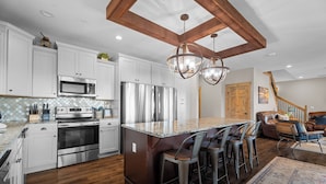 Une cuisine moderne dotée d’appareils électroménagers en acier inoxydable, d’un îlot central en bois avec des tabourets de bar, et d’un escalier menant à une chambre en mezzanine.