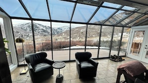 Amplia habitación con techo de cristal, dos sofás de cuero, una mesita redonda y vistas a montañas nevadas.