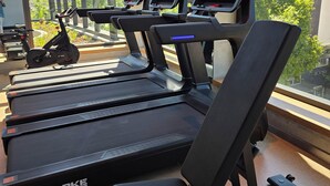 Et fitnesscenter med løbebånd og træningsudstyr, store vinduer samt udsigt til bygninger og træer.