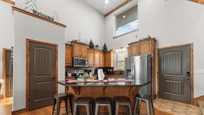 Una cocina con armarios de madera, una isla central con taburetes, un microondas, un refrigerador y una ventana sobre el fregadero.