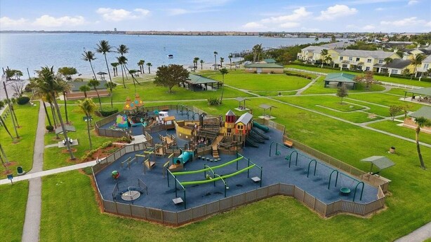 Ein Spielplatz mit verschiedenen Spielgeräten, einem umzäunten Bereich und Blick auf das Wasser.