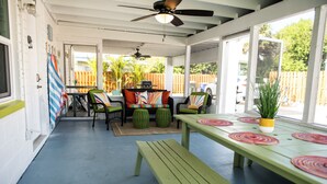 Ein überdachter Patio-Bereich mit einer grünen Bank, zwei Stühlen, einem Tisch mit einem Topfpflanzen und einem Deckenventilator.