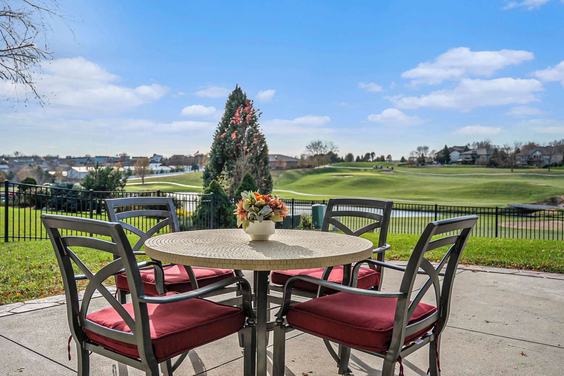 Ein runder Tisch mit vier Stühlen, eine Vase mit Blumen und im Hintergrund eine Aussicht auf einen Golfplatz und Häuser.
