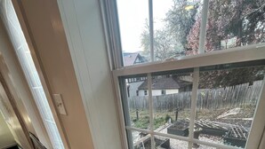 Huone, jossa on ikkuna, josta avautuu näkymä puutarhaan, jossa on kohotettuja kukkapenkkejä ja aita.