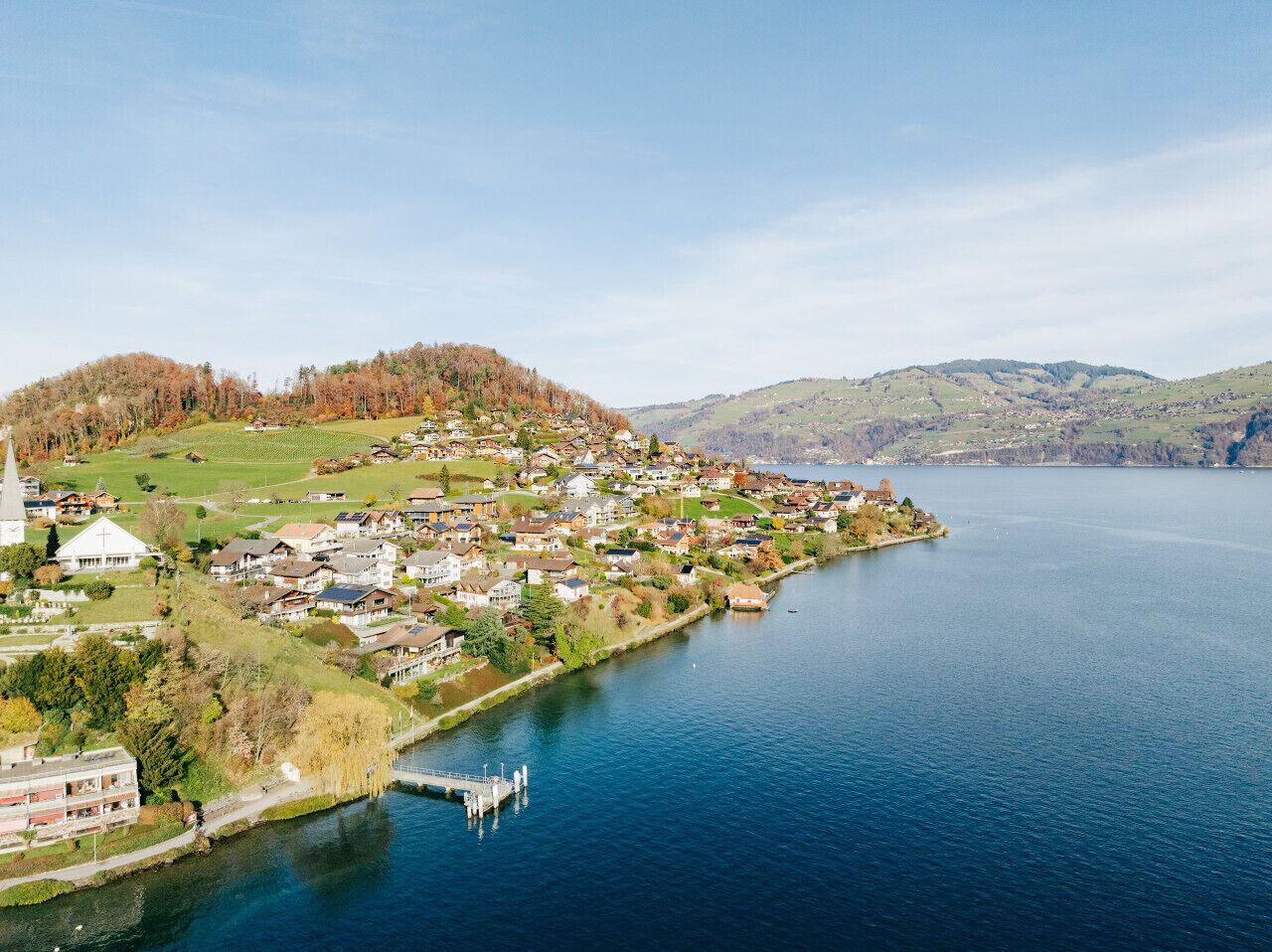 Un pueblo a orillas del lago con una iglesia, edificios residenciales y un muelle.