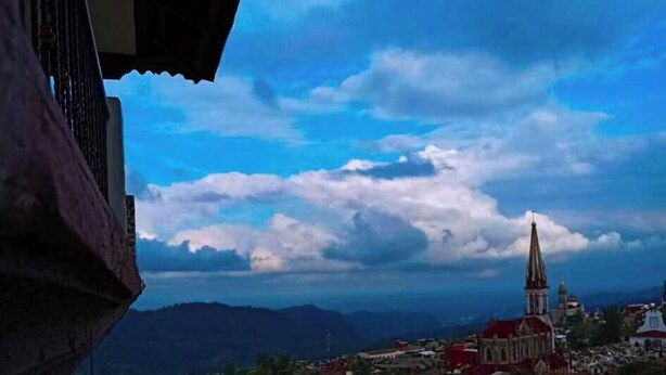 A view of a town with a prominent church spire and mountains in the background. - hotel Posada Jarritos (Cuetzalan del Progreso)