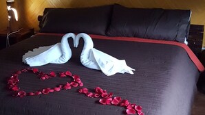 A bed with a dark brown quilt, two white swan-shaped towels, and a red rose petal garland. - hotel Posada Jarritos (Cuetzalan del Progreso)