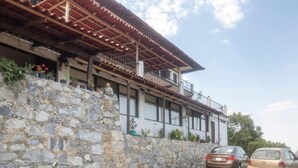 A two-story building with a stone wall and a balcony. There are two cars parked in front. - hotel Posada Jarritos (Cuetzalan del Progreso)