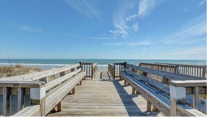 A wooden boardwalk leading to the beach with benches on both sides.