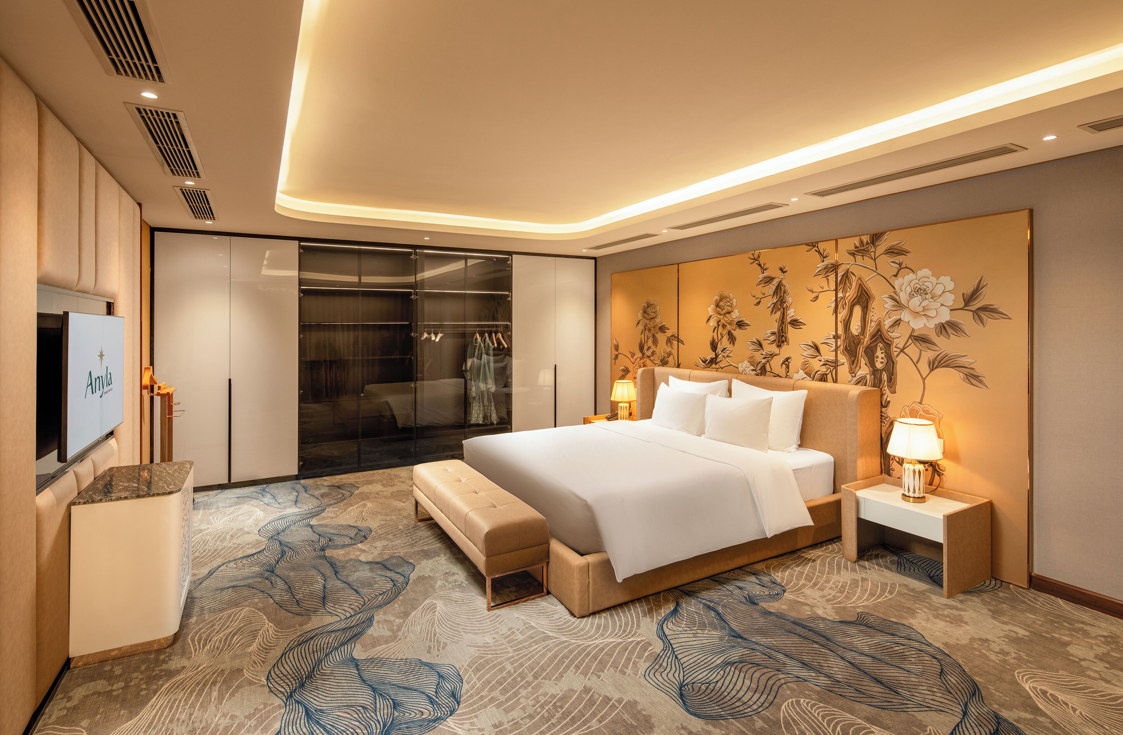 A modern hotel room with a large bed, a walk-in closet, a flat-screen TV, and a decorative wall panel.