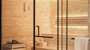 Une salle de bain moderne avec un lambris en bois, une cloison en verre et un porte-serviettes apparent.