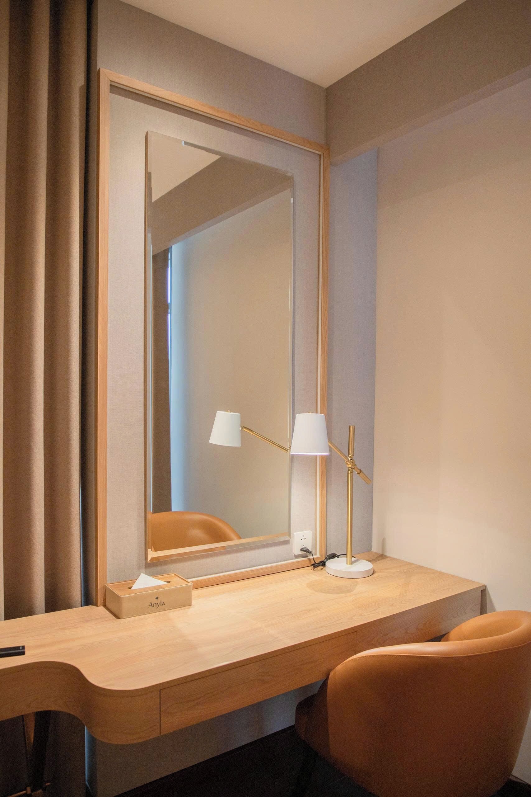 A hotel room with a wooden desk, a mirror, a lamp, and an orange chair.
